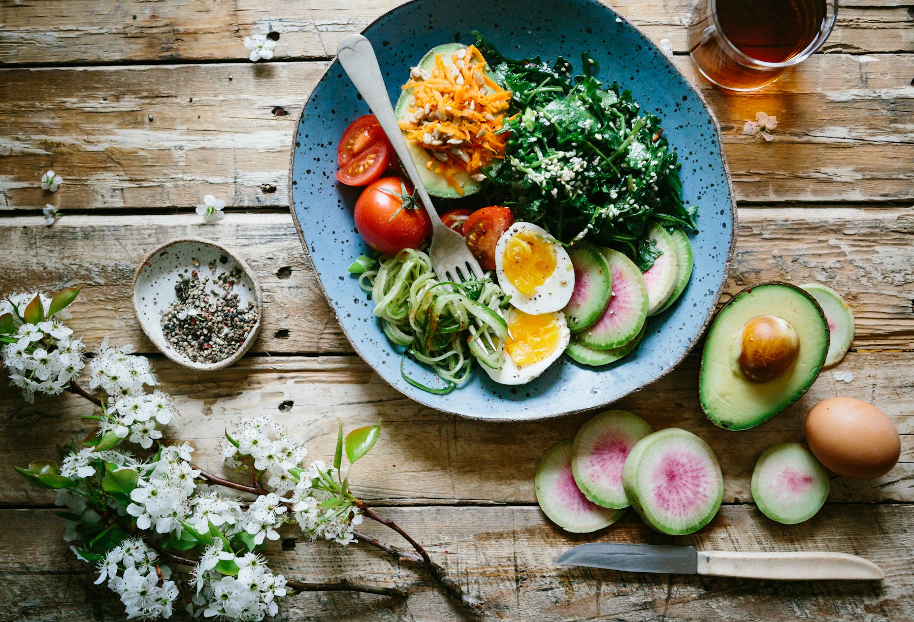 Bunte Schale mit Gemüse, Avocado und Ei auf einem Holztisch